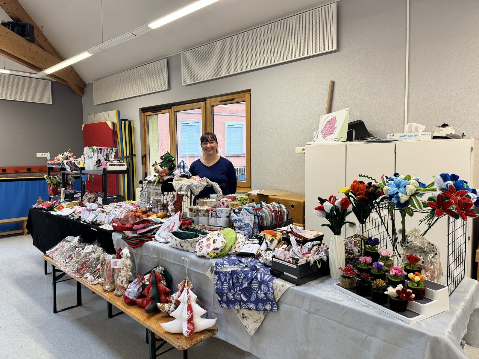 Salle de l’exposition artisanale, tables garnies de créations de Noël