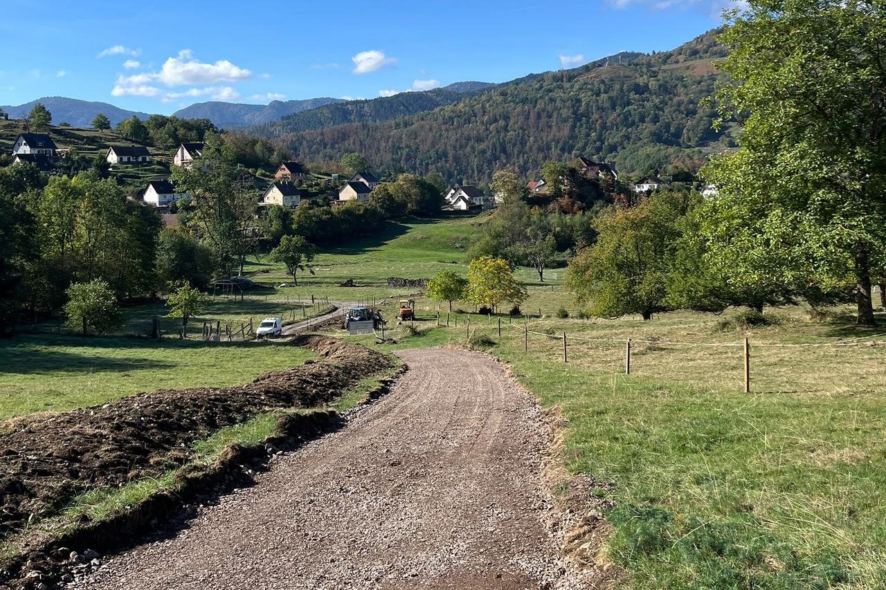 Chemin empierré descendant à travers un pré, le village en arrière-plan