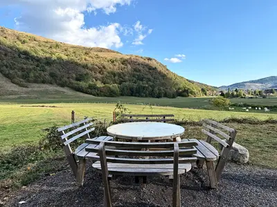 Table ronde et bancs de bois au bord du pré, face au versant